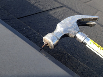 長生郡一宮町　棟板金の浮いた釘を金槌で打ち込んでいる