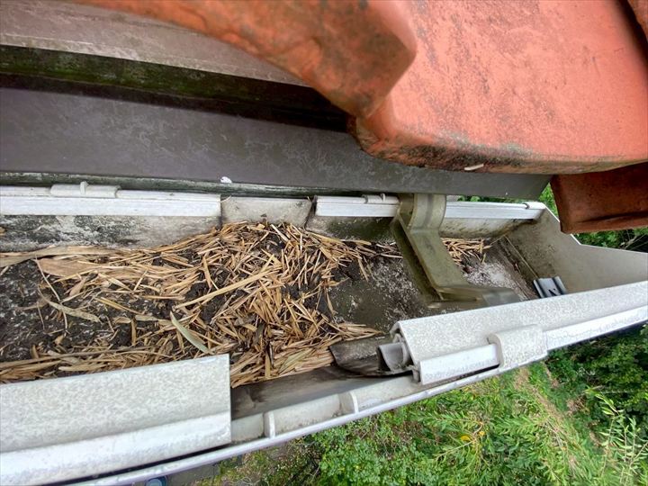 現場を確認すると、軒樋の内部には土や枯れ草、竹の葉のような植物片が堆積していました。これらが排水口（集水器）を塞いでおり、水がスムーズに流れない状態です。放置すると、雨水が屋根や外壁を伝ってしまい、雨漏りや外壁劣化につながる恐れがあります。